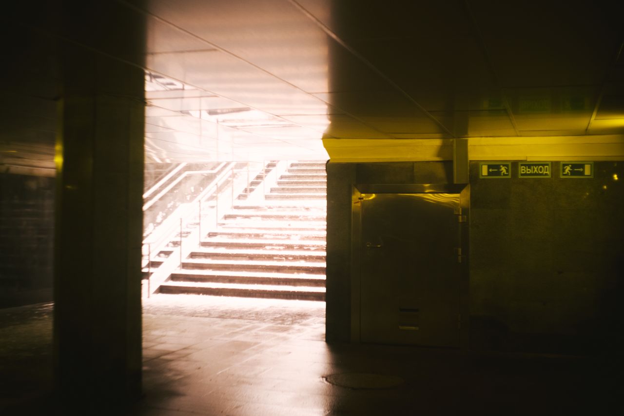 A shadowy underground subway entrance illuminated by sunlight filtering down the steps.