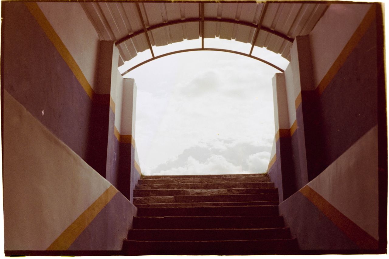 Architectural stairs leading to a bright, cloudy sky, framed by colorful walls.
