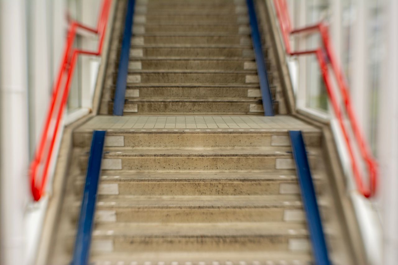 Concrete stairs with red and blue metal railings in an indoor setting.