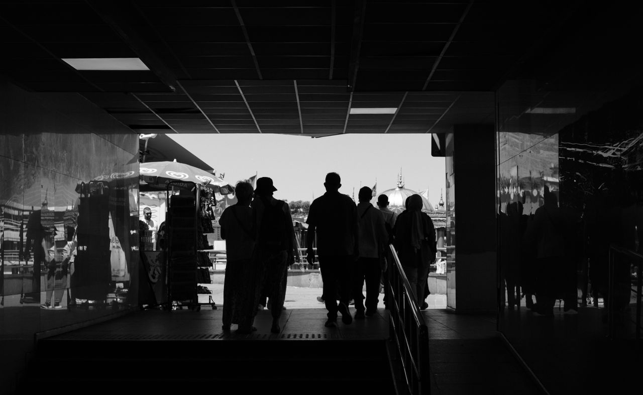 Silhouettes of people exiting an underground passage to a sunlit outdoor area.